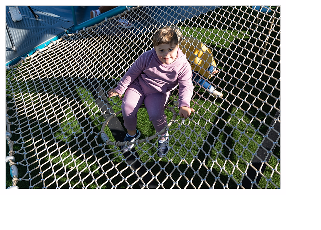 Child sitting with legs through porthole on climbing net