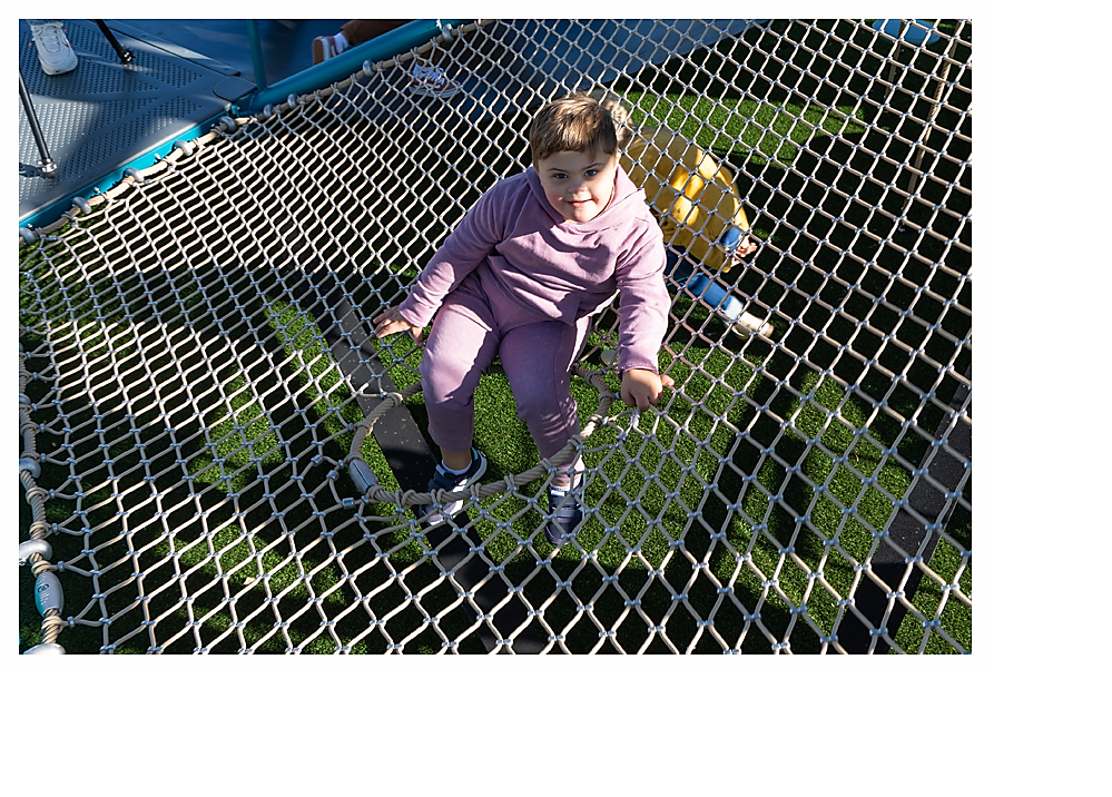 Child sitting with legs through porthole on climbing net